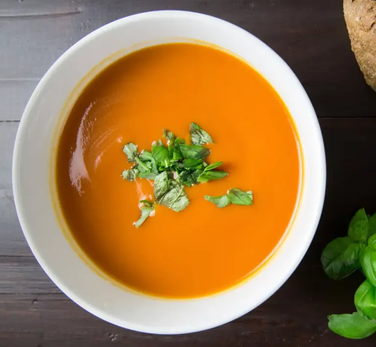 Smooth creamy homemade tomato soup in a white bowl garnished with fresh basil