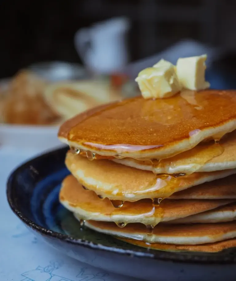 Stack of thick, fluffy IHOP-style copycat pancakes with butter pats on top and maple syrup drizzling down the sides