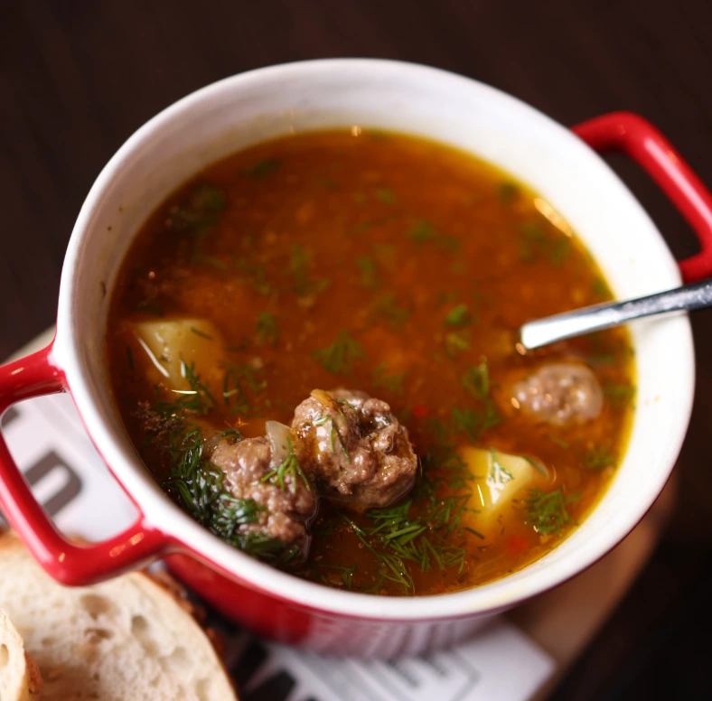 Homemade meatball soup with potatoes and fresh dill, served with crusty bread