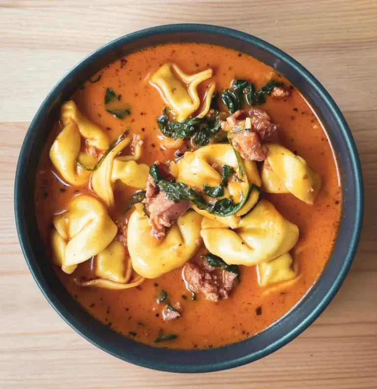 Bowl of rich tomato-cream tortellini soup with crumbled Italian sausage, plump cheese tortellini, and wilted spinach